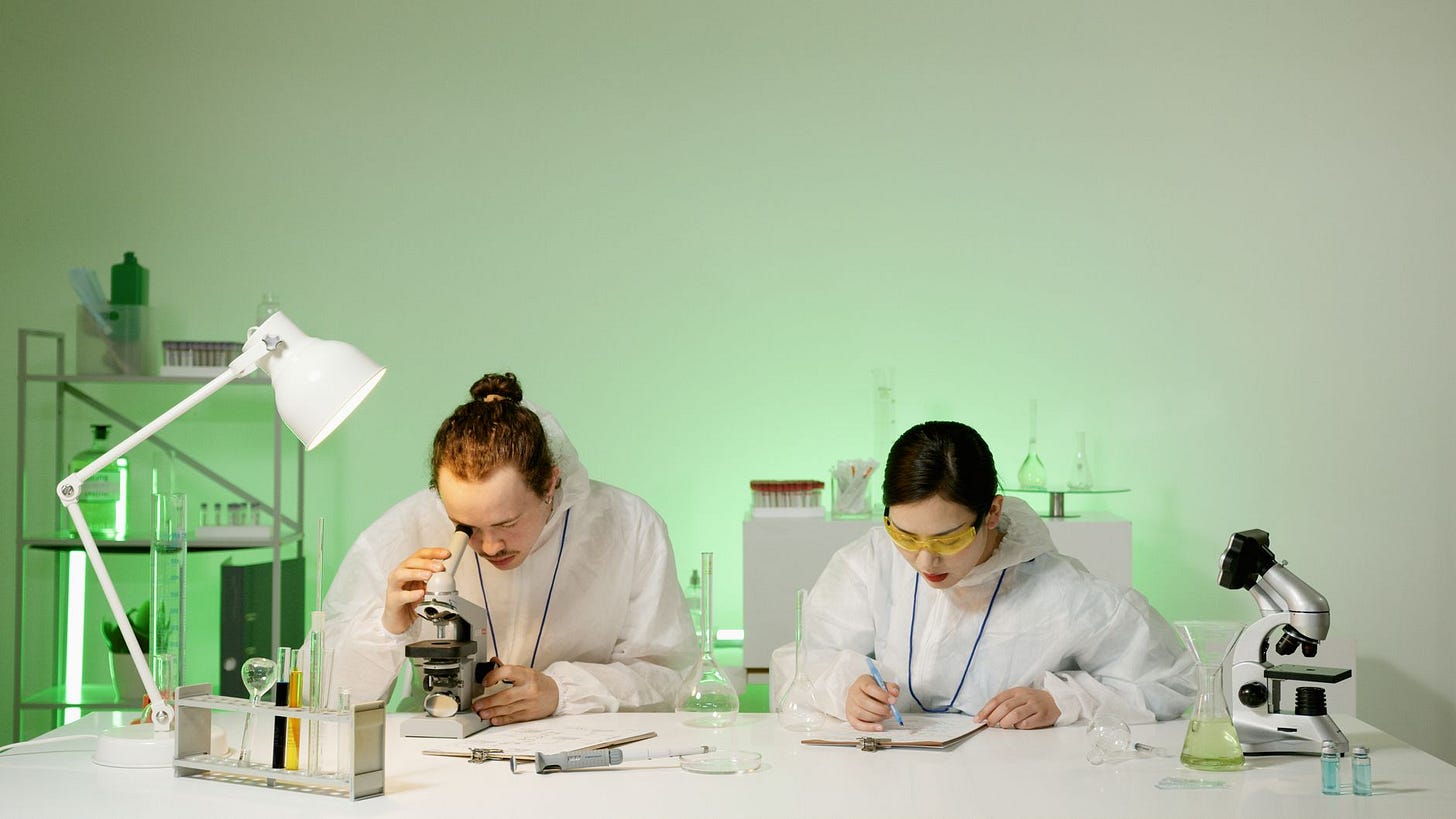 Photo by Artem Podrez on Pexels Two scientists in protective suits working with microscopes and notes in a laboratory setting. (stock photo)