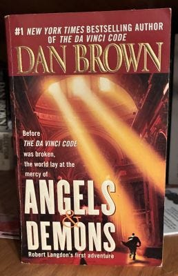 Angels & Demons by Dan Brown, shows a shadow figure of a man running in what looks like a chapel.