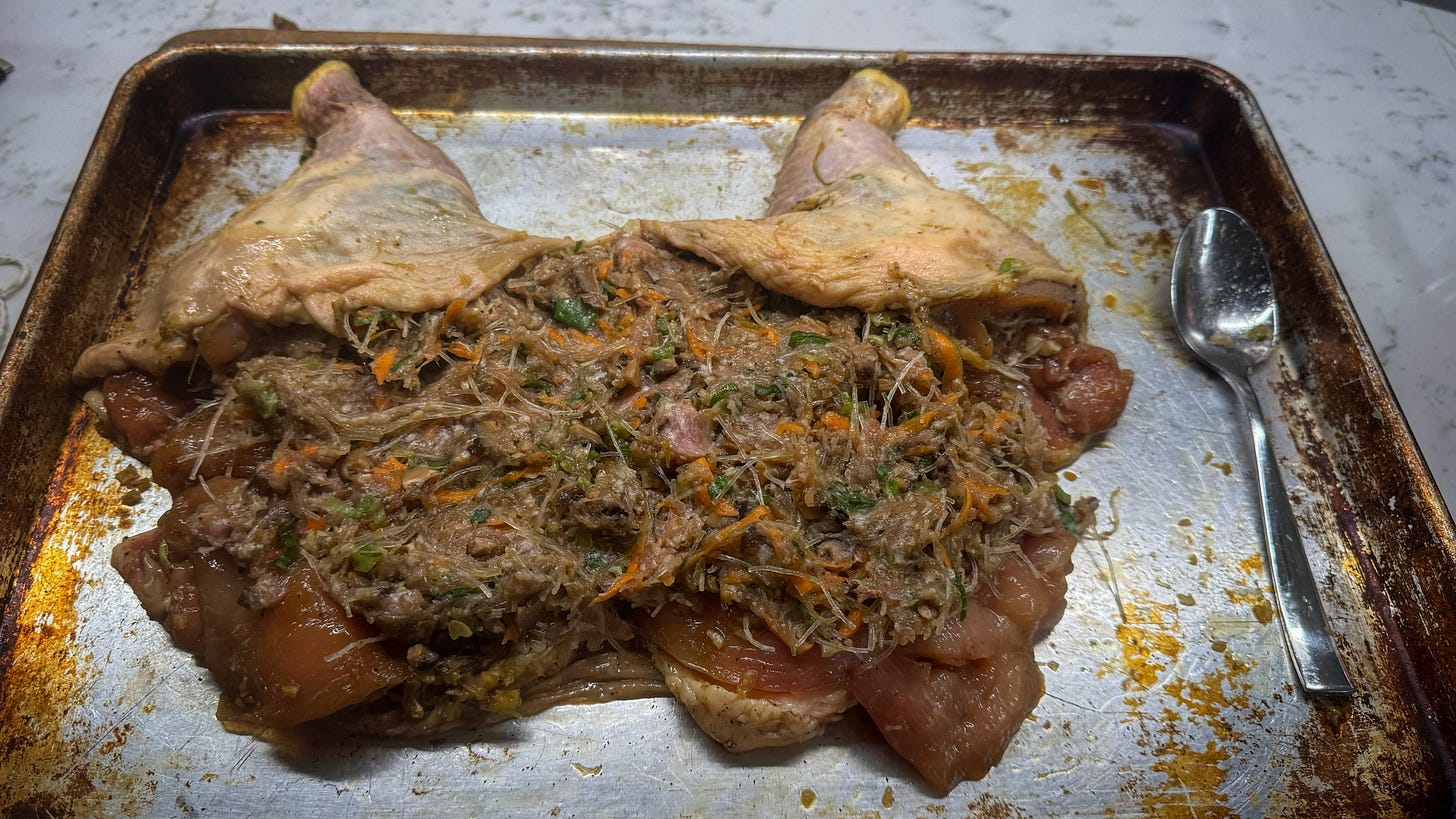 A deboned chicken on a sheet pan, covered in a stuffing of glass noodles, ground pork, vegetables, and seasoning.