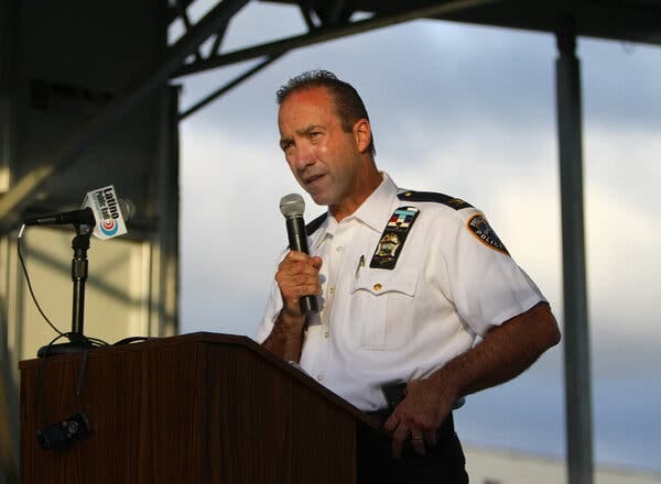 Hugh T. Clements Jr. stands at a podium in a police uniform holding a microphone. Hugh T. Clements Jr. stands at a podium in a police uniform holding a microphone.