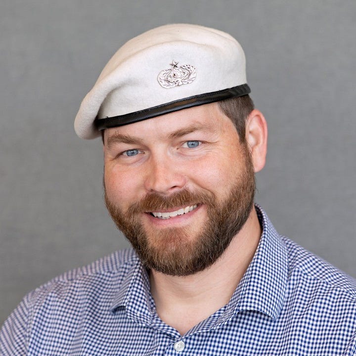 A close-up portrait of Edward Hood smiling wearing his white beret with the 1D7X1W badge and a blue checkered button-up shirt, set against a plain gray background. The other picture is his official military portrait.