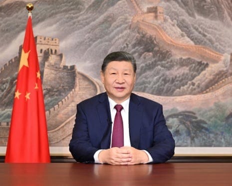 Chinese President Xi Jinping sitting at a desk in front of a painting of the Great Wall and next to a Chinese flag