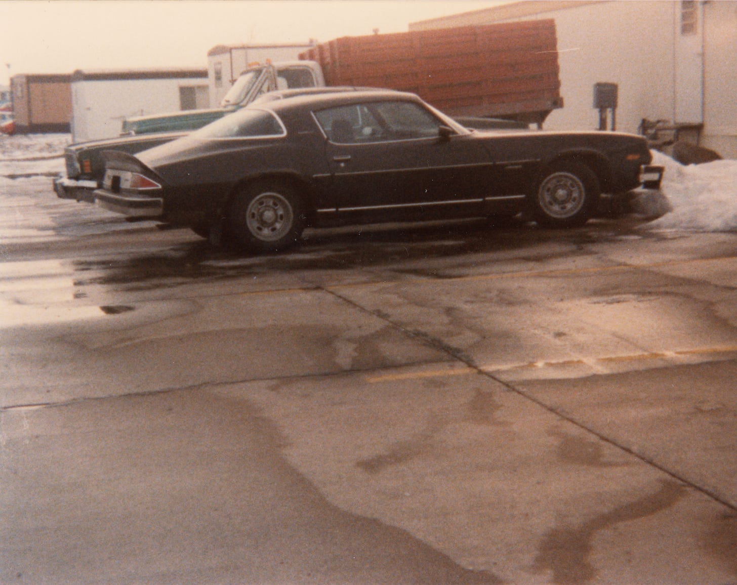 black muscle car parked outside a trailer in snowy weather