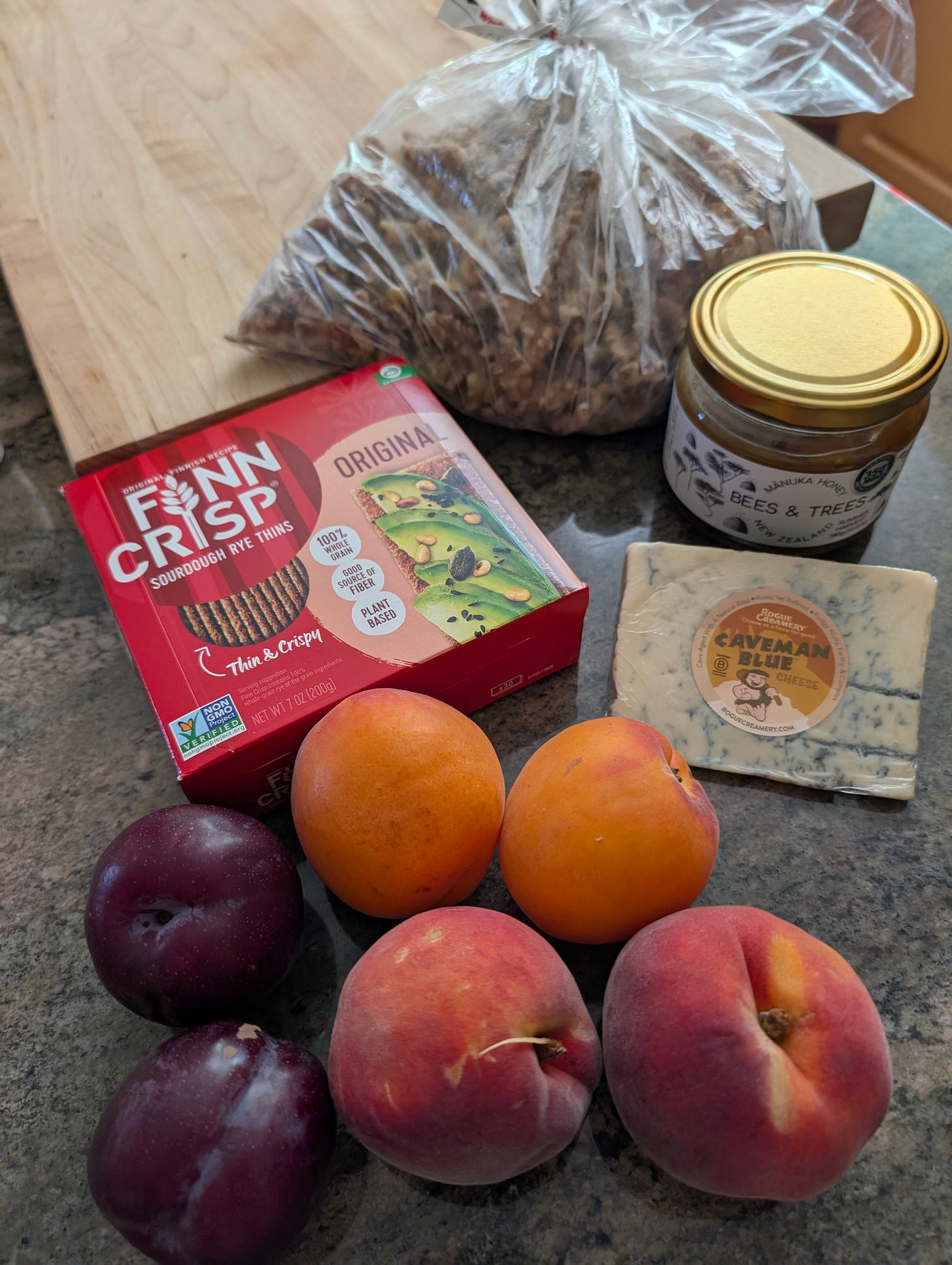 peaches, plums, apricots, crackers, jar of honey and bag of walnuts on a wood cutting board