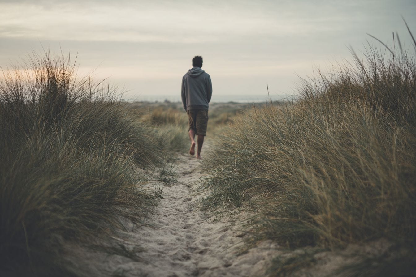 Homme marchant pieds nus sur un chemin de sable entre les dunes, évoquant la présence incarnée et le retour à soi Homme marchant pieds nus sur un chemin de sable entre les dunes, évoquant la présence incarnée et le retour à soi