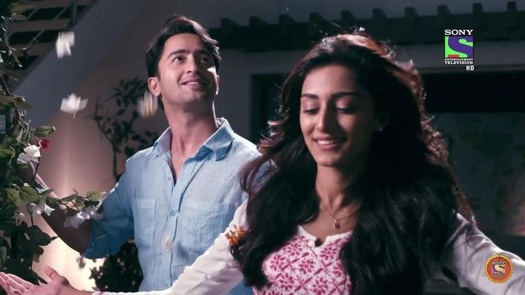 This may contain: a man and woman standing next to each other in front of a tree with flowers on it