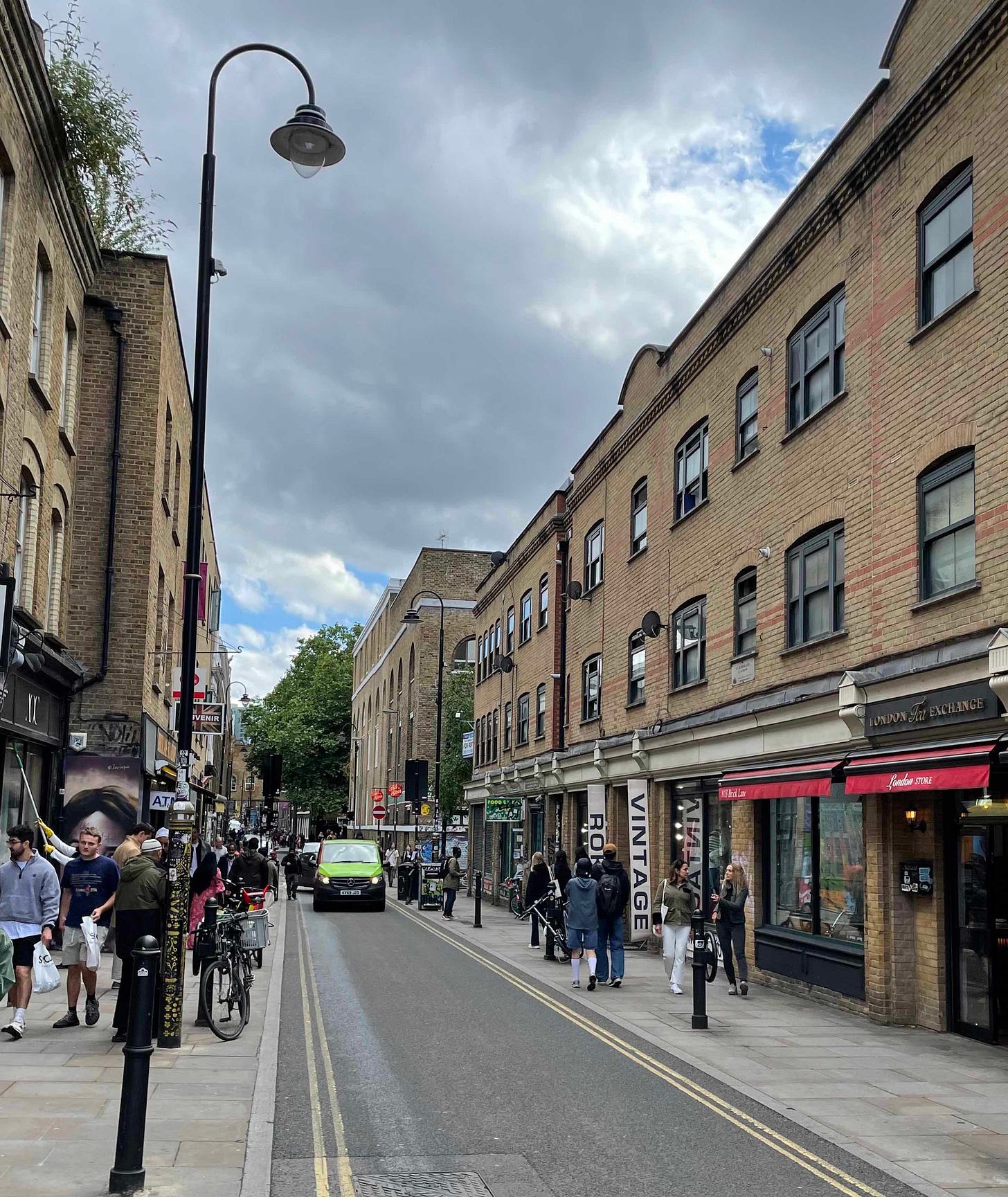 Colour photo of Brick lane in east London with shops, cars and people walking 