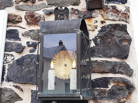 Outside of the stone Dobbin House restaurant; a welcome sign for the Springhouse Tavern and a closeup of candle-style lighting/ A sign for the Slave Hideout Museum, and a display of 3 slaves hiding in a crawl space. The owner of the restaurant stands in front of a huge stone fireplace in a room set up as a colonial kitchen.