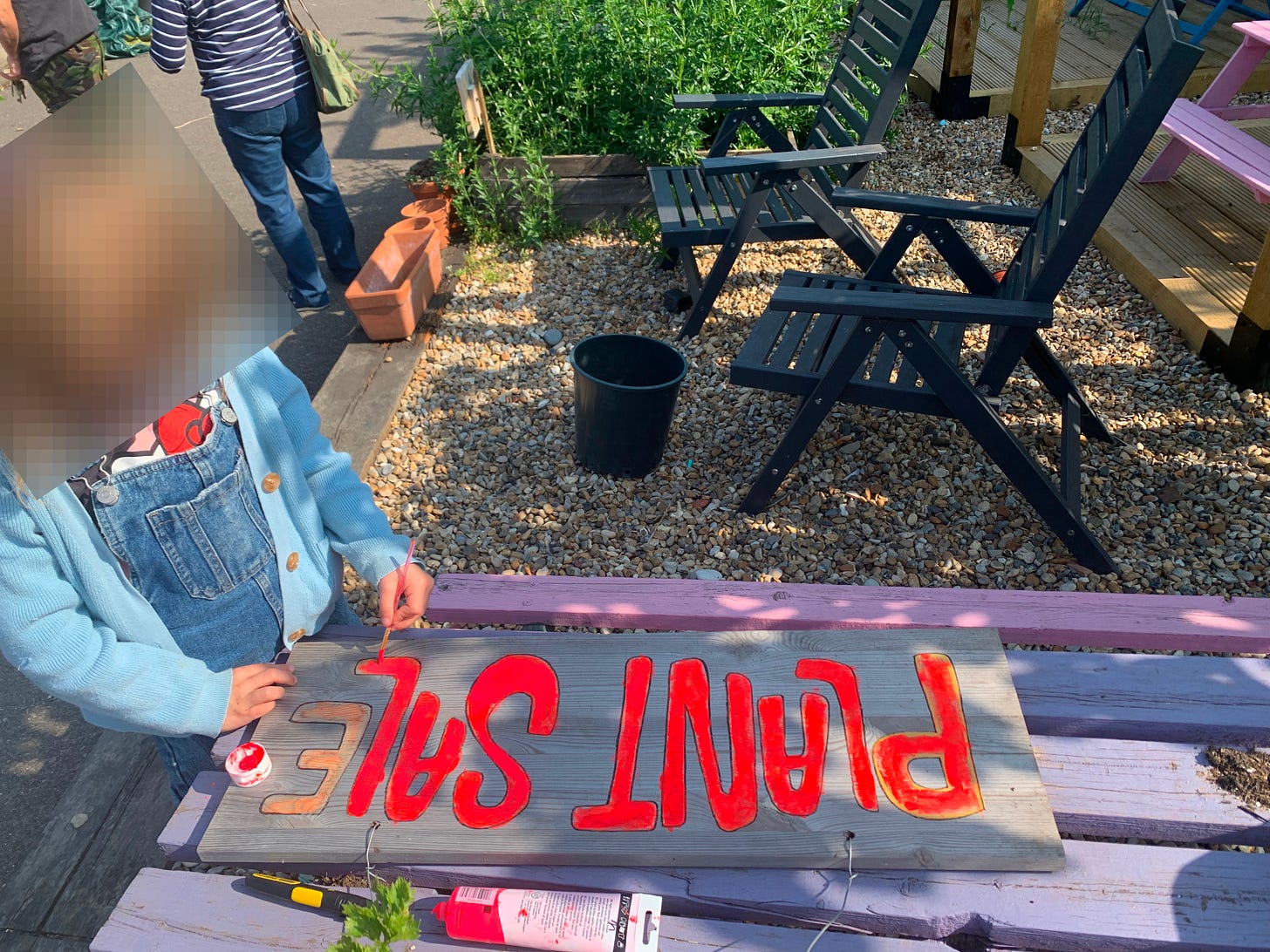 Young volunteer repaints an old sign saying "PLANT SALE"