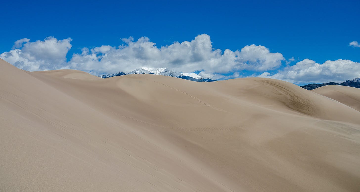 Sand dunes below mountains covered in snow.