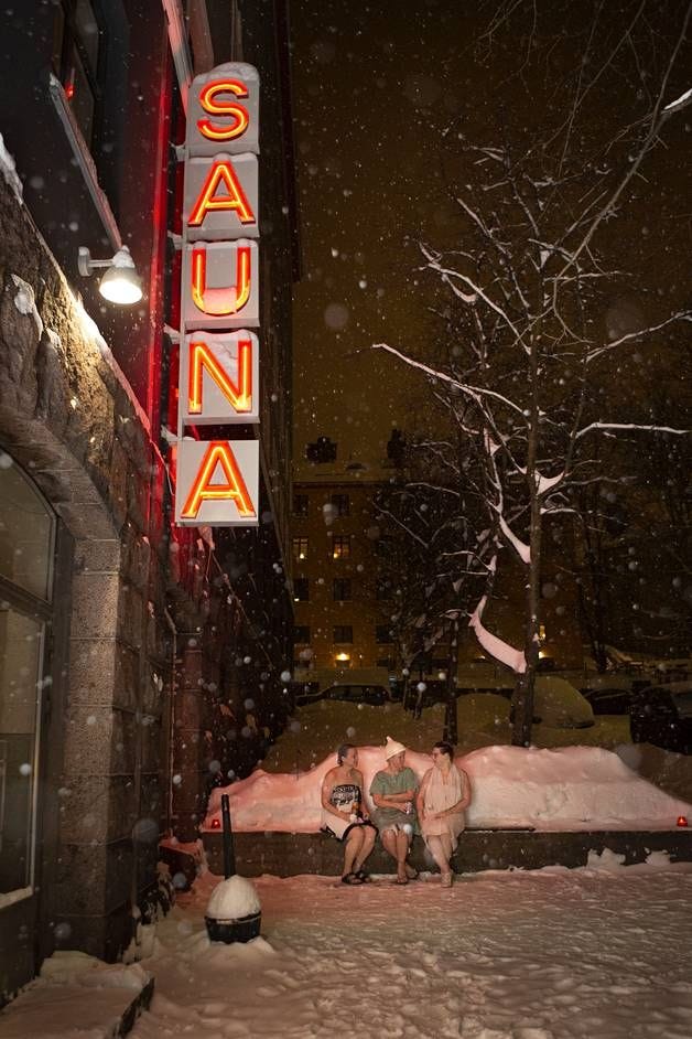 This may contain: people sitting on a bench in the snow under a neon sign that reads sauna This may contain: people sitting on a bench in the snow under a neon sign that reads sauna