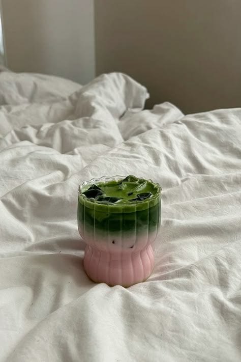 This may contain: a pink and green cup sitting on top of a white bed covered in sheets,