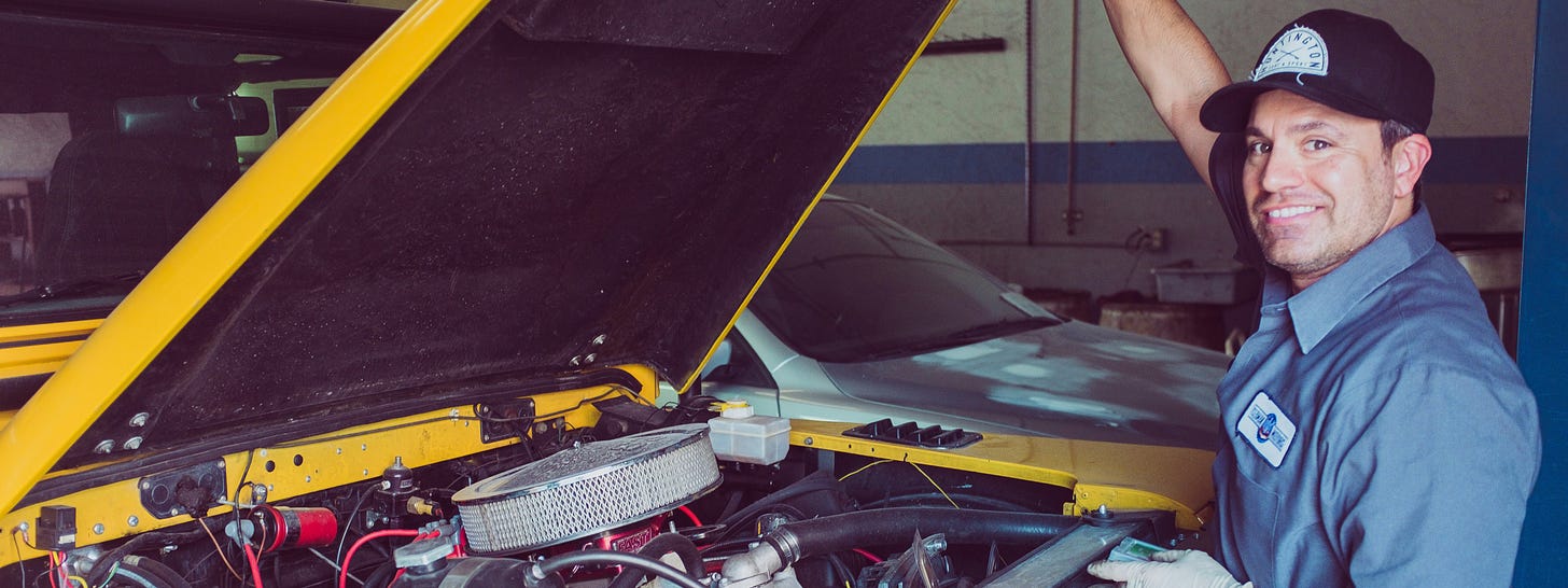 Old-style mechanic posing in front pf the open hood of a car with the engine exposed Old-style mechanic posing in front pf the open hood of a car with the engine exposed