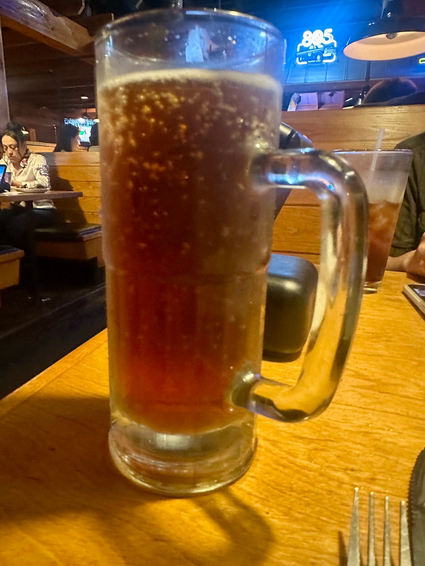 A tall mug of beer with bubbles attached to the side of a glass, in a booth at Texas Roadhouse