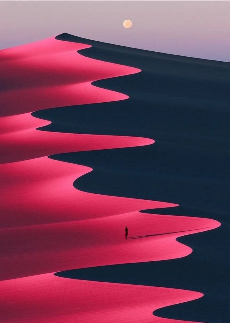 A lone figure walks along red-hugged sand dunes that make a patter like waves or a snake that weaves toward the full moon in the distance A lone figure walks along red-hugged sand dunes that make a patter like waves or a snake that weaves toward the full moon in the distance