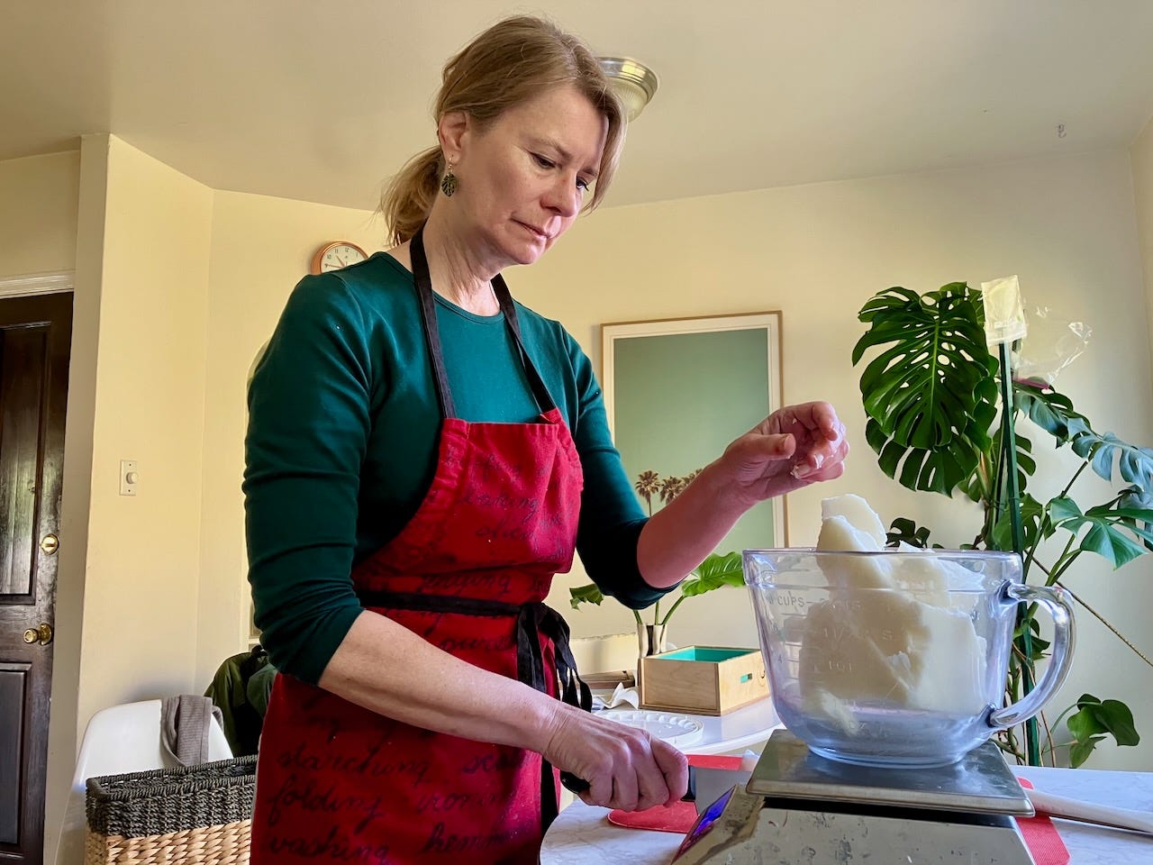 Julia Scheeres stands at a table, weighing soap ingredients on a kitchen scale.