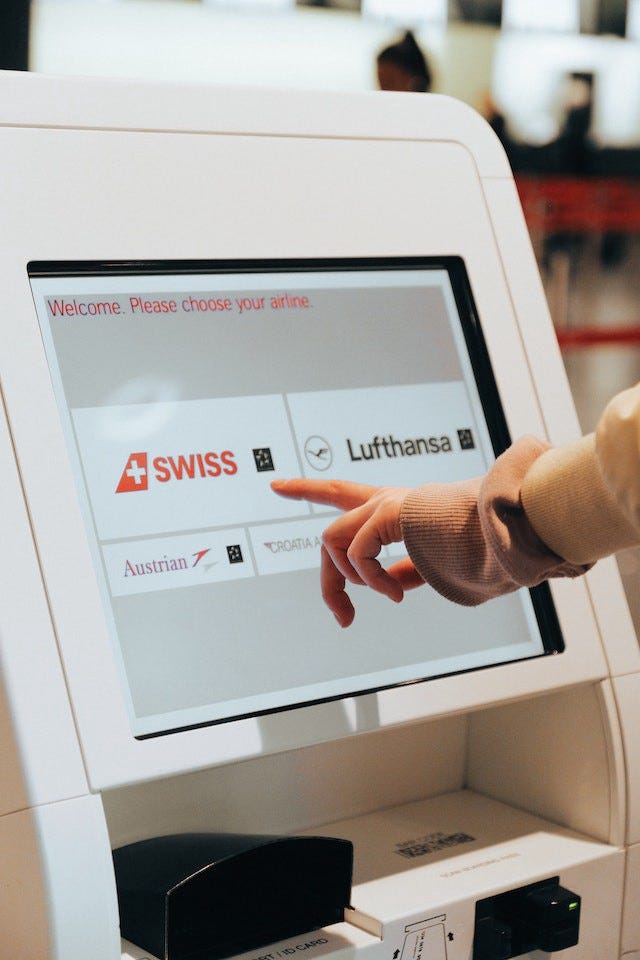 A hand pointing towards one of 5 airlines shown on a screen. It is a touch-screen kiosk for easy airline check-in. A hand pointing towards one of 5 airlines shown on a screen. It is a touch-screen kiosk for easy airline check-in.
