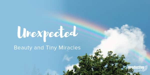 Blue sky with a rainbow running through a cloud, a treetop is at the bottom of the frame. Text overlay: Unexpected Beauty and Tiny Miracles Blue sky with a rainbow running through a cloud, a treetop is at the bottom of the frame. Text overlay: Unexpected Beauty and Tiny Miracles