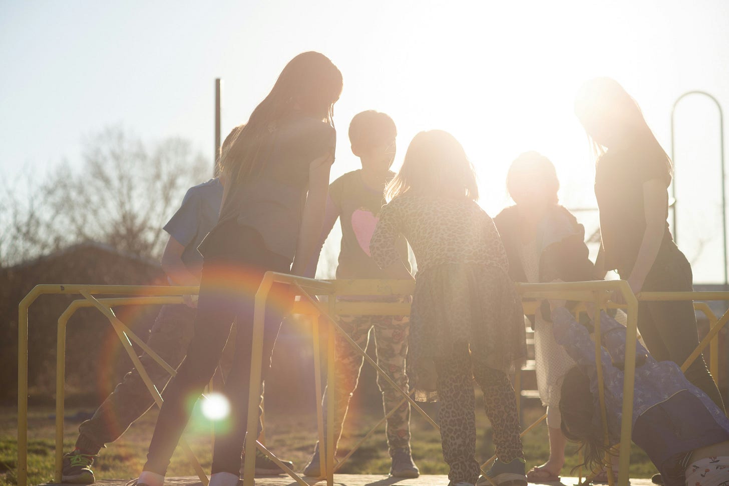 Color photo of a group of kids on a vintage playground merry-go-round with the sun shining through them