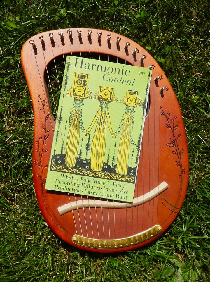 Harmonic Content zines photographed outdoors, held against autumn trees and resting on a wooden stringed instrument in grass.