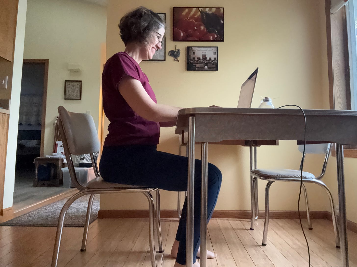A woman sits at a kitchen table with hands on the keyboard