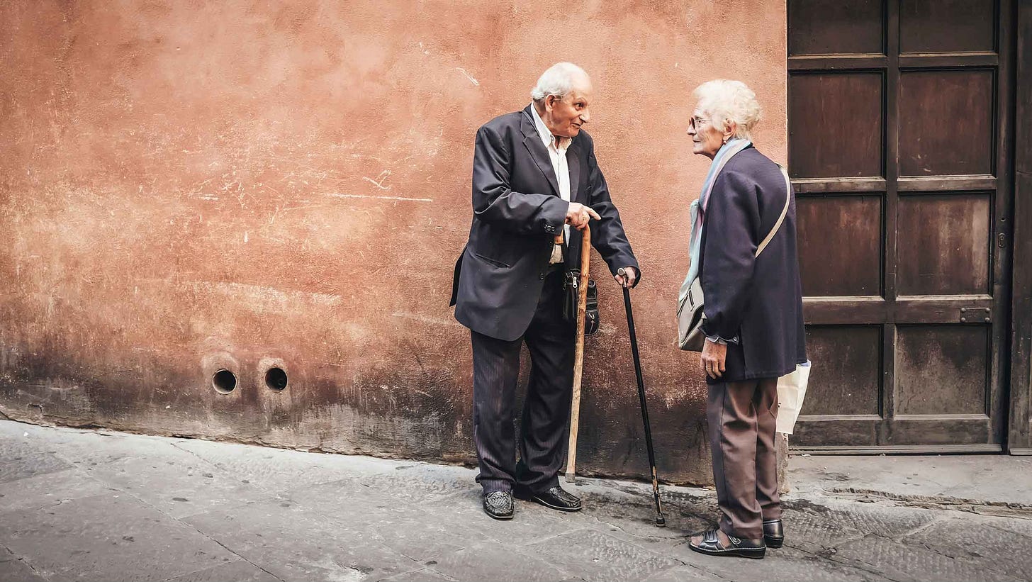 An elderly man with a cane talking with an elderly woman on a street