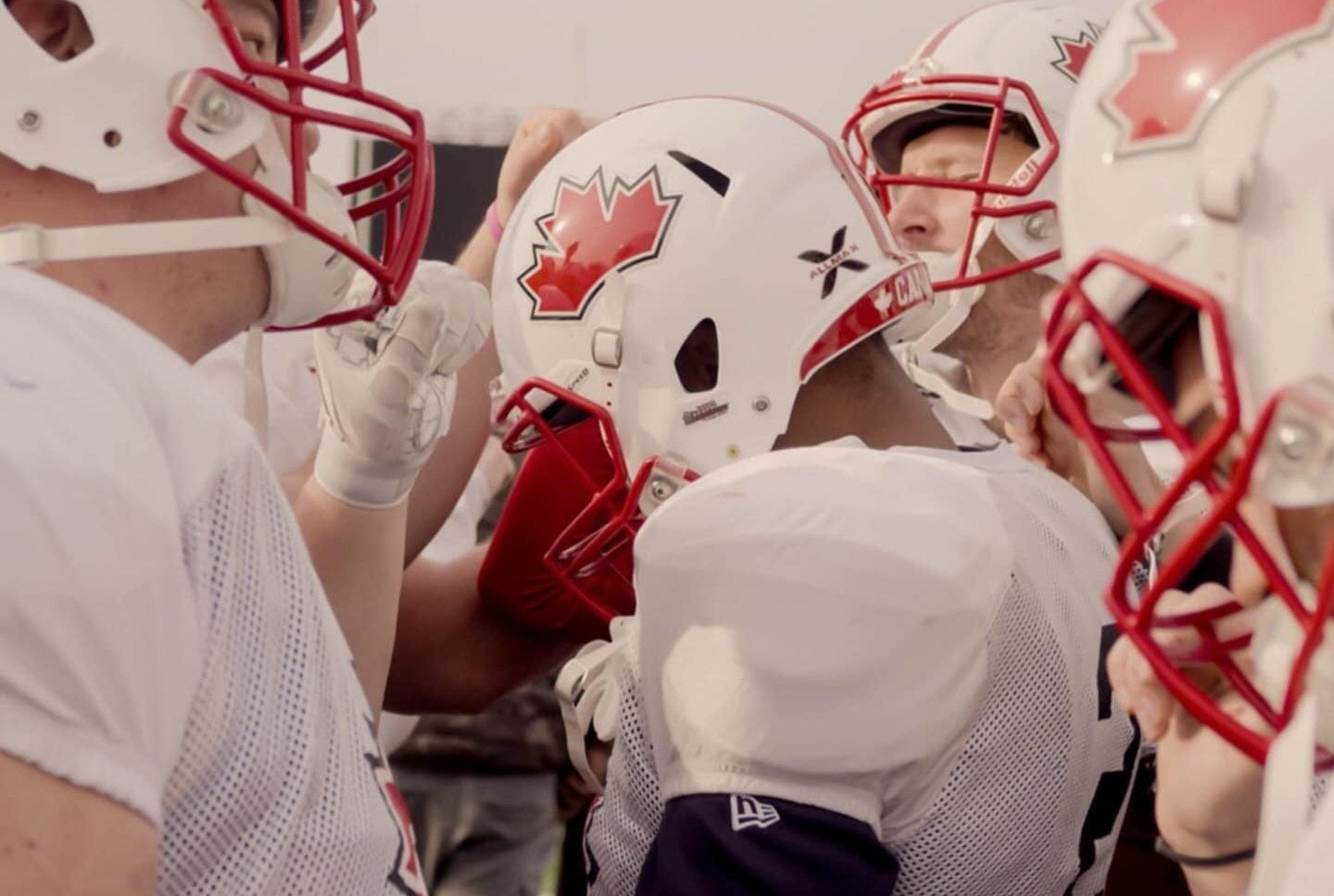 Football players wearing white practice uniforms and white helmets with a red maple leaf on the side and a red facemask, put their fists into a huddle Football players wearing white practice uniforms and white helmets with a red maple leaf on the side and a red facemask, put their fists into a huddle