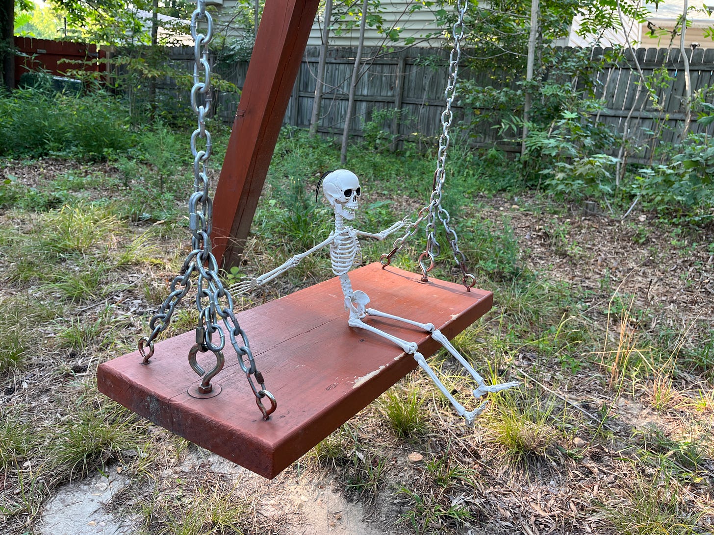 A photo of a toy skeleton sitting on a wooden swing seat in an overgrown backyard.