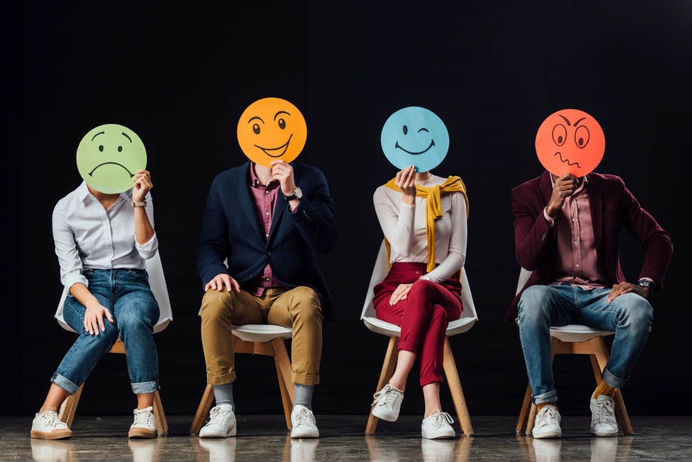 Photo of people holding round hand-drawn faces over their own faces, each depicting an emotion