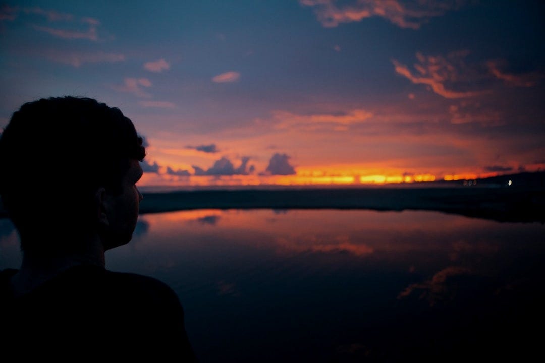 person standing near sea under cloudy sky person standing near sea under cloudy sky