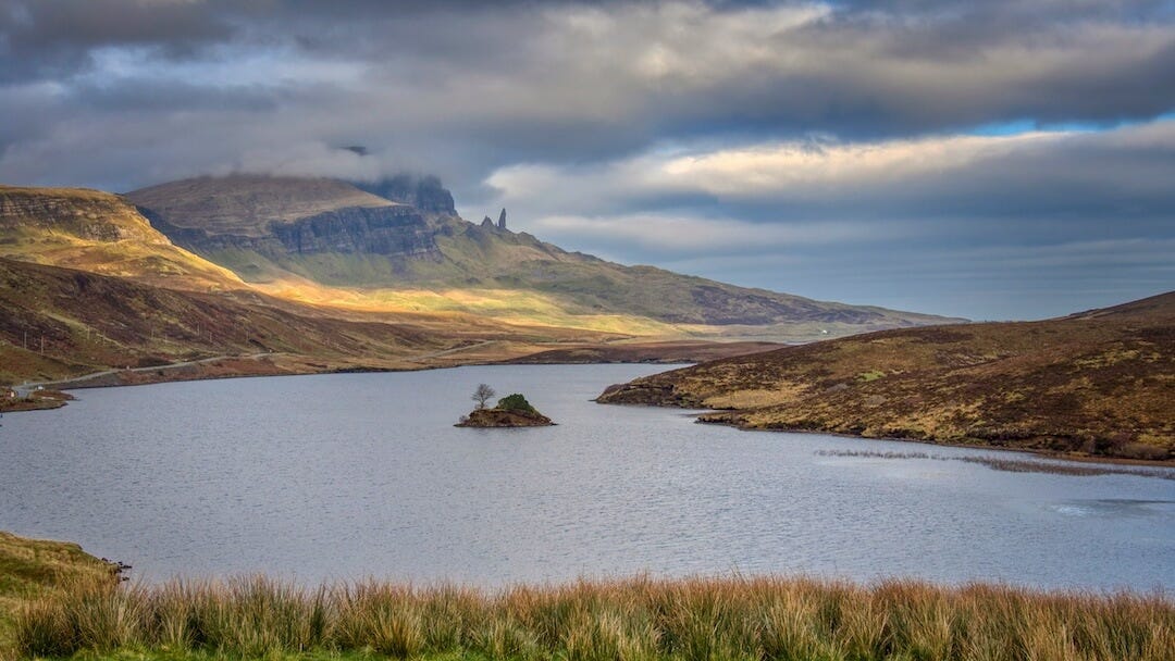 View across a loch and its island toward a ridge and rocky pinnacles