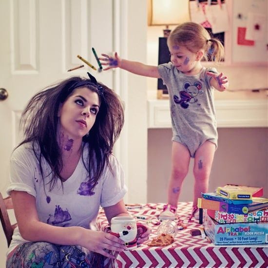 This may contain: a woman sitting at a table with a child standing on top of her and holding scissors
