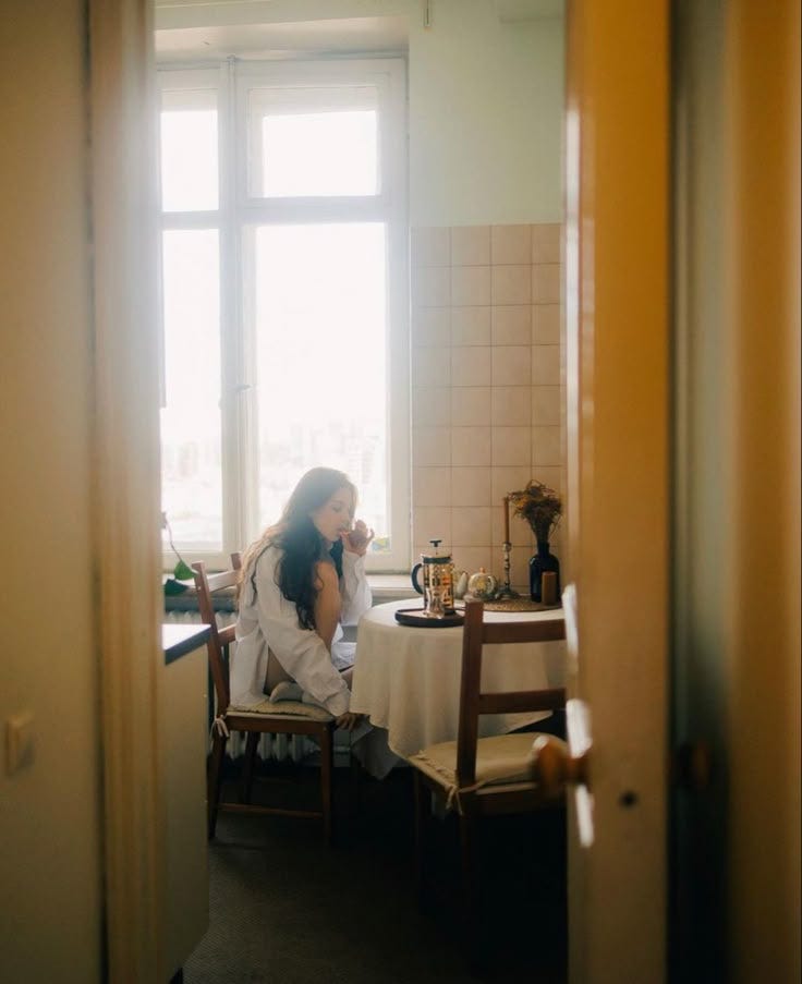This may contain: a woman sitting at a table in front of a window