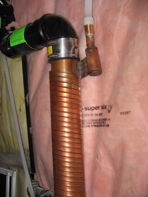 A coil of copper tubing wraps repeatedly around a plumbing pipe. Water flowing through the tube exits out the top into the plastic PEX cold water intake line A coil of copper tubing wraps repeatedly around a plumbing pipe. Water flowing through the tube exits out the top into the plastic PEX cold water intake line