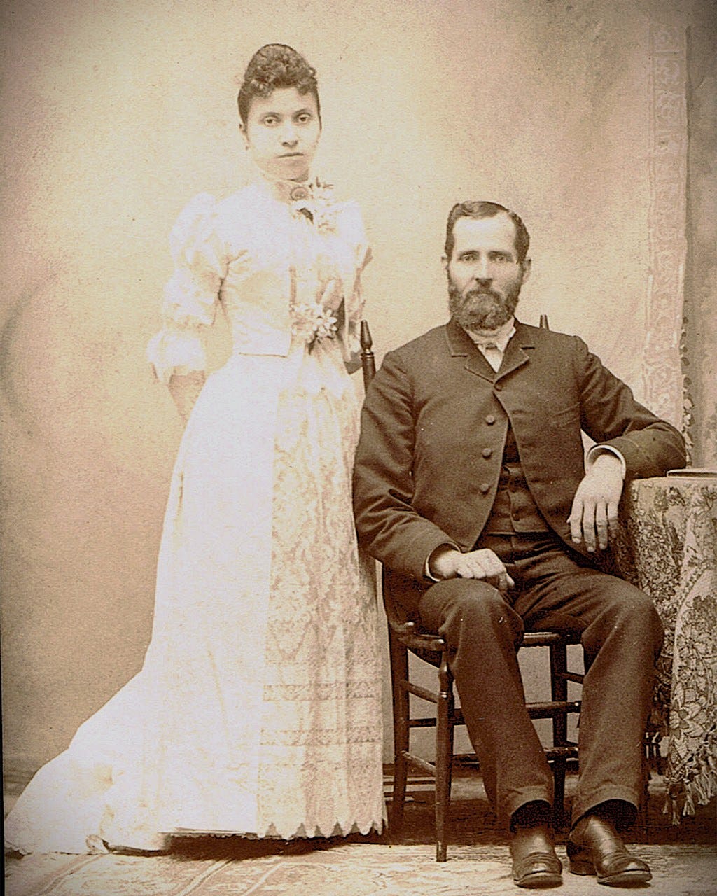 Studio portrait of Julia Yesler Benson Intermela standing beside her husband Charles Intermela, who is seated.