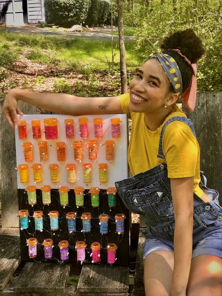 Kiana from 2020 with artwork inspired by bipolar disorder that she painted. A black and white canvas with rainbow painted pill bottles