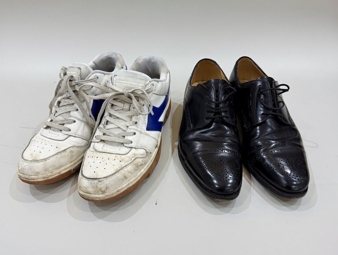 A pair of worn, scuffed white trainers next to polished black brogues, representing the contrast between people who’ve done the hard work of building and those who look the part.