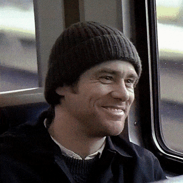 a man wearing a beanie is smiling while sitting in a car