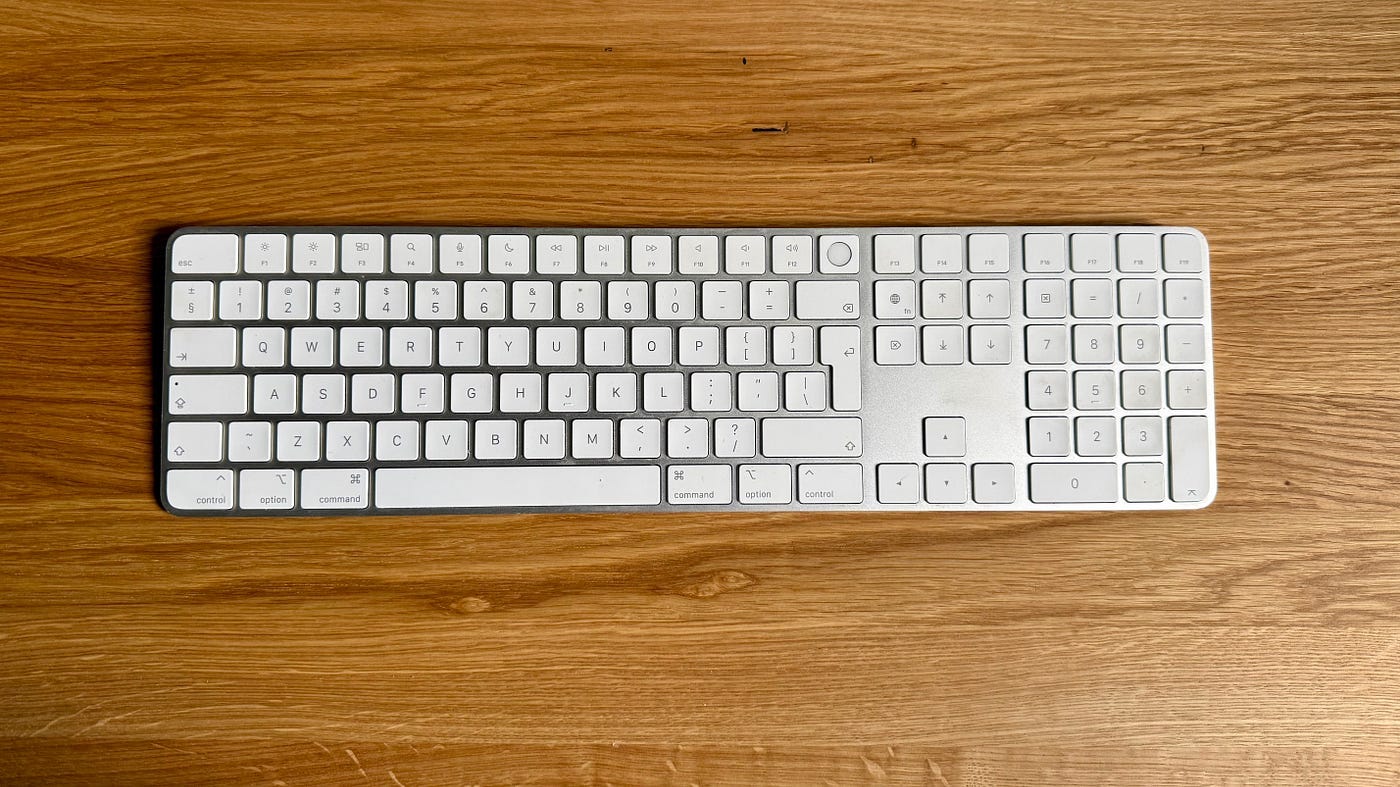 Apple Magic Keyboard with numeric keypad on wooden desk, wireless Bluetooth keyboard for Mac setup.