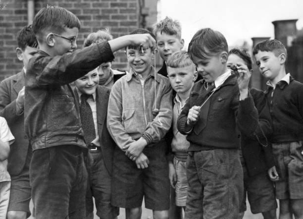 People, Children, pic: September 1952, Great Britain, Boys playing "conkers" in the street with other gathered around watching