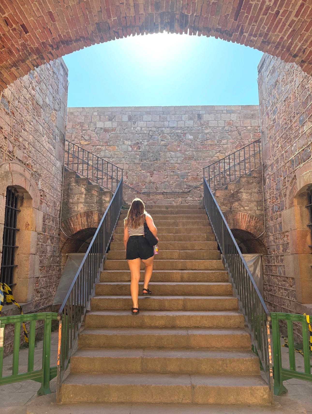 A woman walks up a wide stone staircase framed by brick arches and old stone walls.