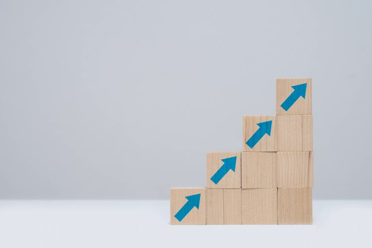 Wooden blocks stacked in ascending order with blue arrows, representing growth, progress, and success against a minimalistic background.