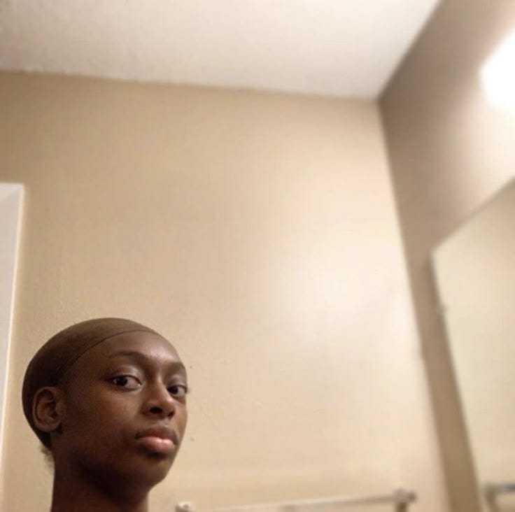 This may contain: a woman standing in front of a bathroom mirror with her hair pulled back and looking at the camera