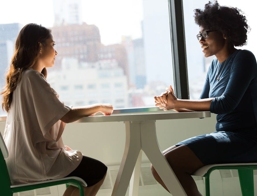 two women sitting beside table and talking
