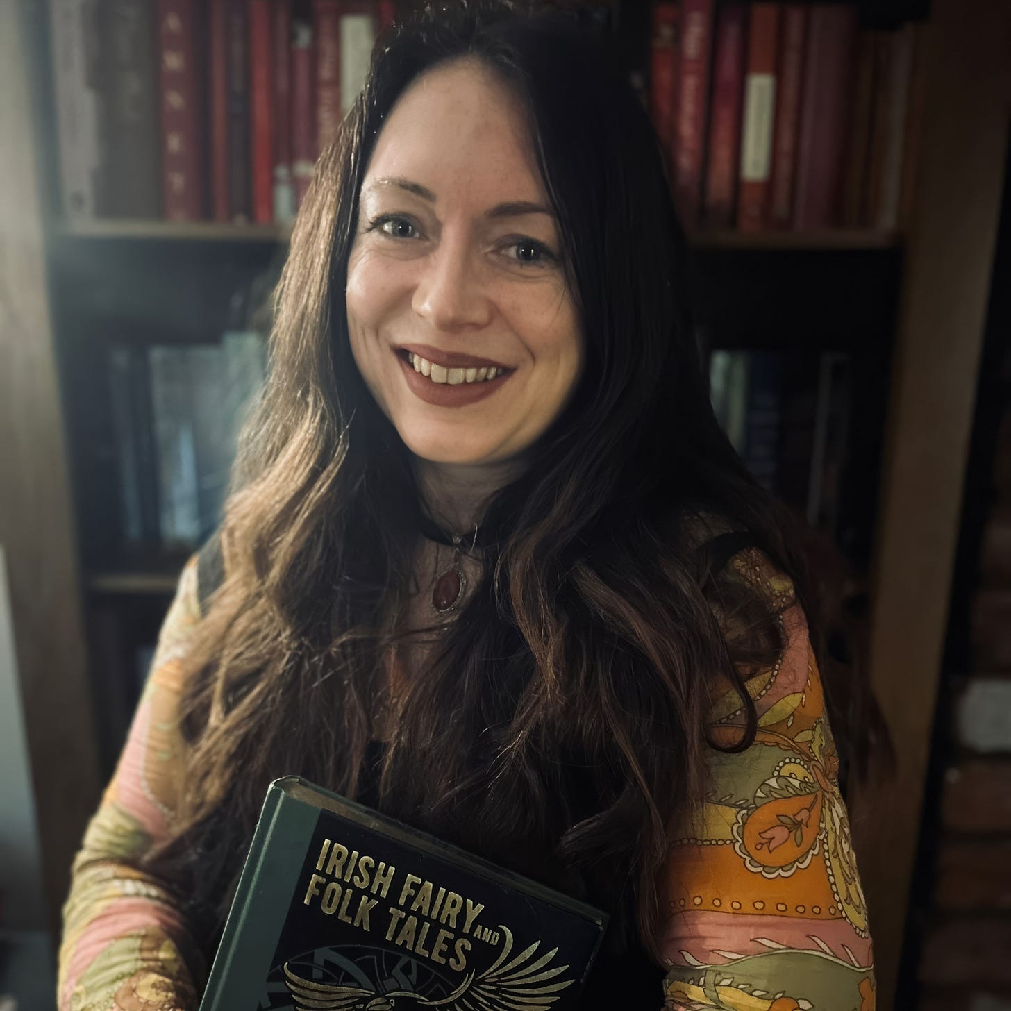 Marie Waller holding Irish Fairy and Folk Tales book in front of bookshelf - writer of Ghost of a Smile exploring folklore, ghosts and uncanny history in Tarot DMs interview. Marie Waller holding Irish Fairy and Folk Tales book in front of bookshelf - writer of Ghost of a Smile exploring folklore, ghosts and uncanny history in Tarot DMs interview.