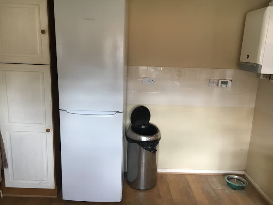 Original kitchen before the renovation Tall fridge freezer by the side of a single cupboard and bare wall