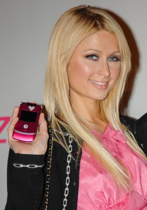 Blonde woman holds up a pink flip phone.