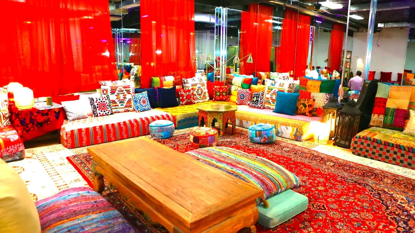 Colorful interior of The Chai Spot Pakistani tea lounge in Little Italy Manhattan, with floor seating, cushions, rugs, tapestries, and handmade goods creating a cozy living room atmosphere