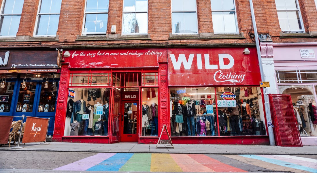 The Wild Clothing shop with a red shopfront, two shops either side, and a rainbow painted on the path in front of it