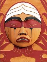A wooden mask with a carved face. The face has closed eyes, a downturned mouth, and red and black painted features. White paint forms a headband-like design above the eyes, and red and black patterns extend downward from the eyes like tears.